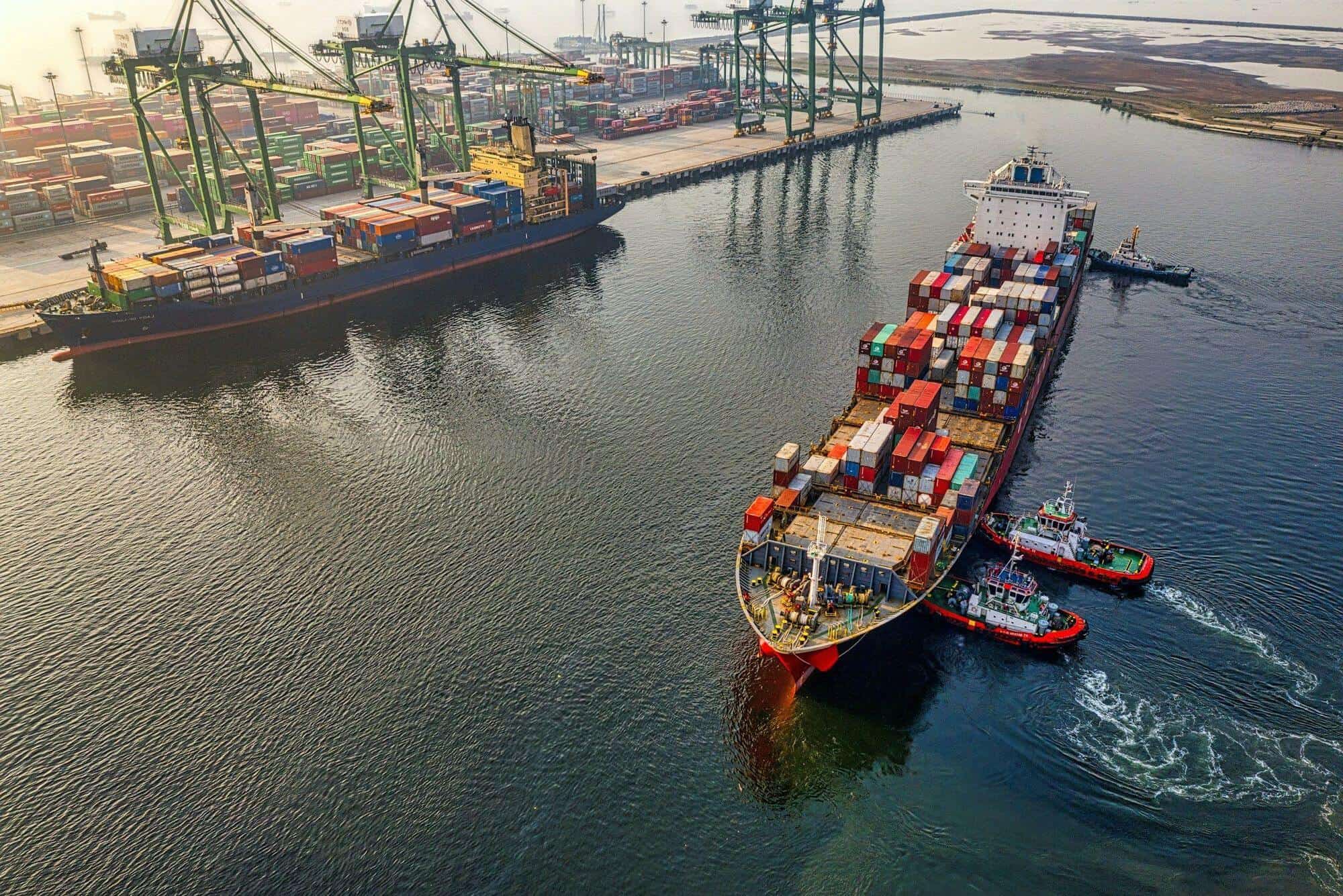 Container ship guided into port by tugboats at dawn